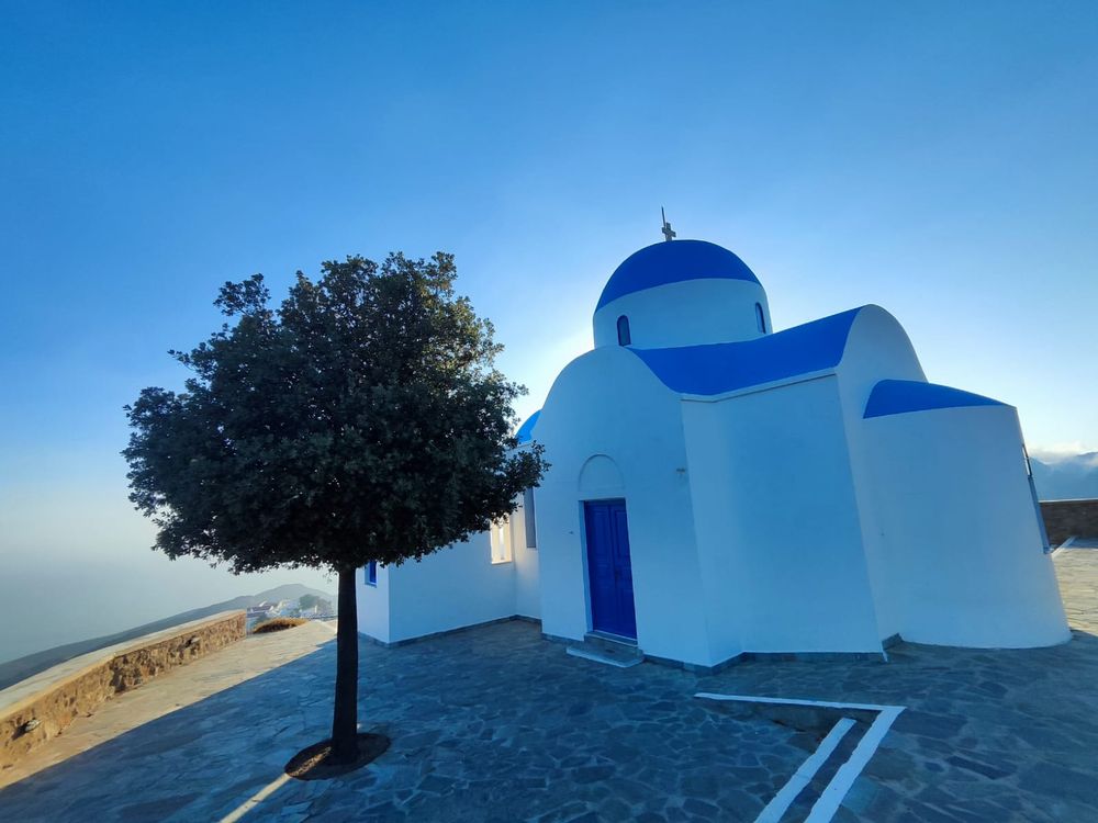 Weiße Kirche mit blauer Kuppel und Olivenbaum in der Ägäis